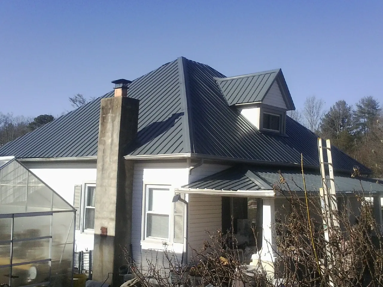 Dark blue standing seam metal roof on a white farmhouse with dormer — Slate & Tile Roof Repair by Roofing Brothers in Mc Bain