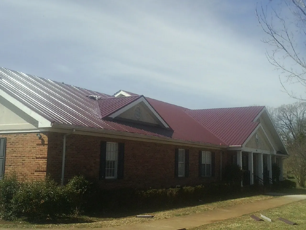 Red metal roof with gabled entries on a long brick building, from a Hail Damage Roof Repair job in Mc Bain