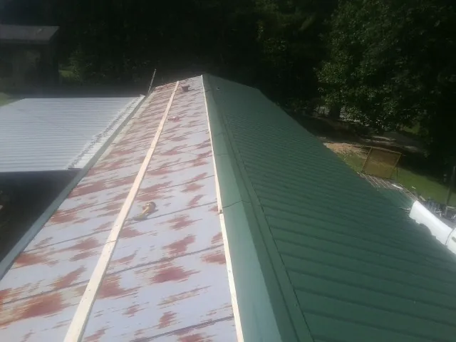 Old rusted panels beside newly installed green metal roofing — Wind Damage Roof Repair by Roofing Brothers in Mc Bain
