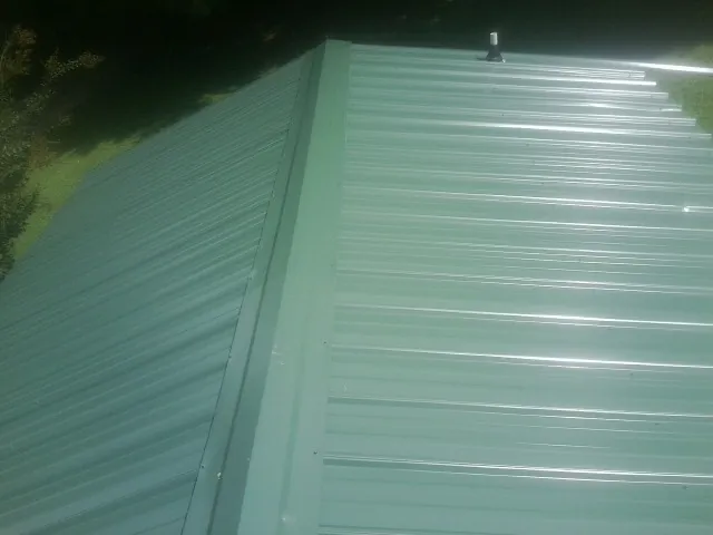 New green metal panels meeting at the ridge of a roof — Flat Roof Repair work by our crew in Mc Bain
