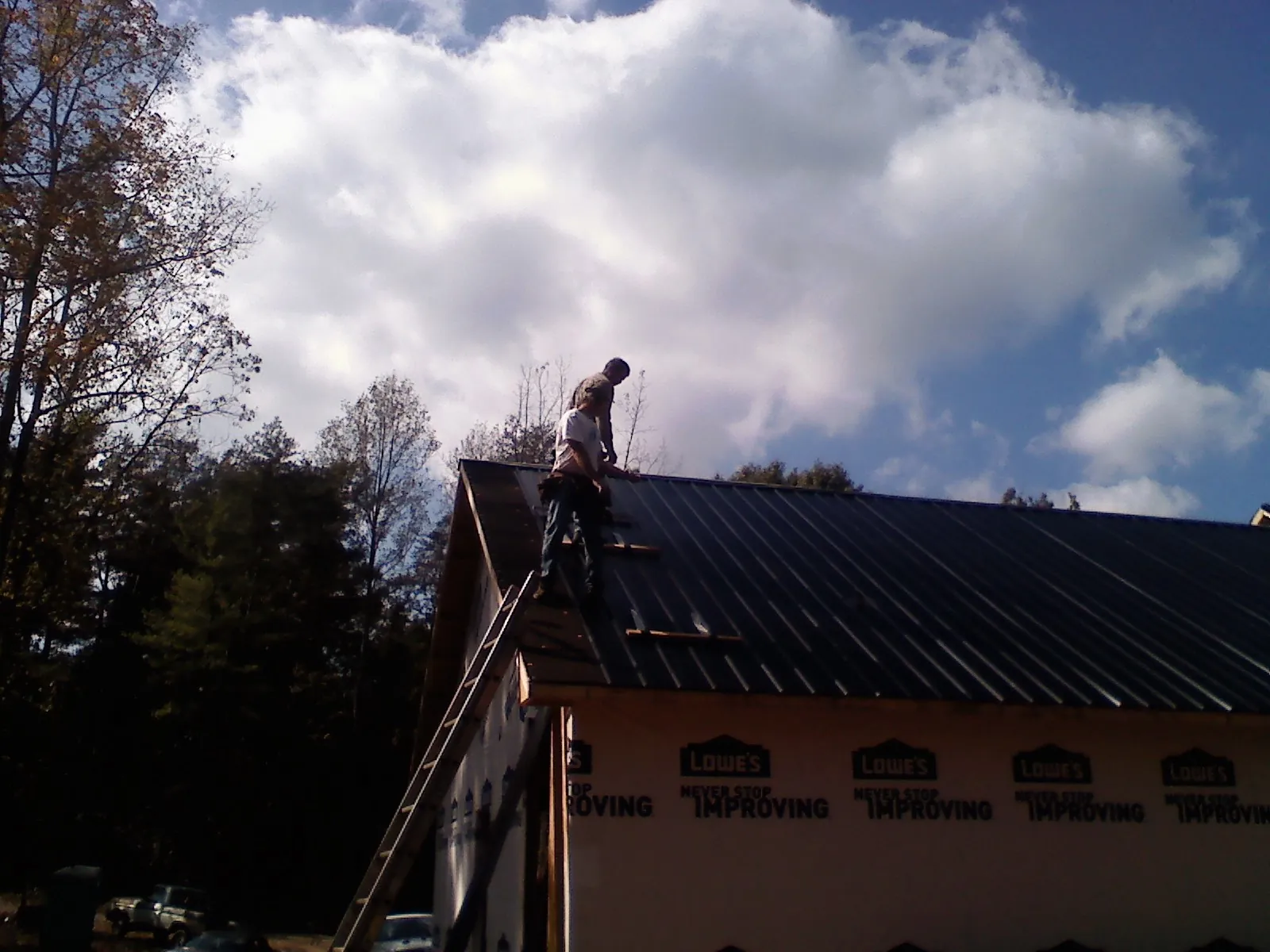 Roofer fastening dark metal panels high against a cloudy sky, from a Roof Inspection job in Mc Bain