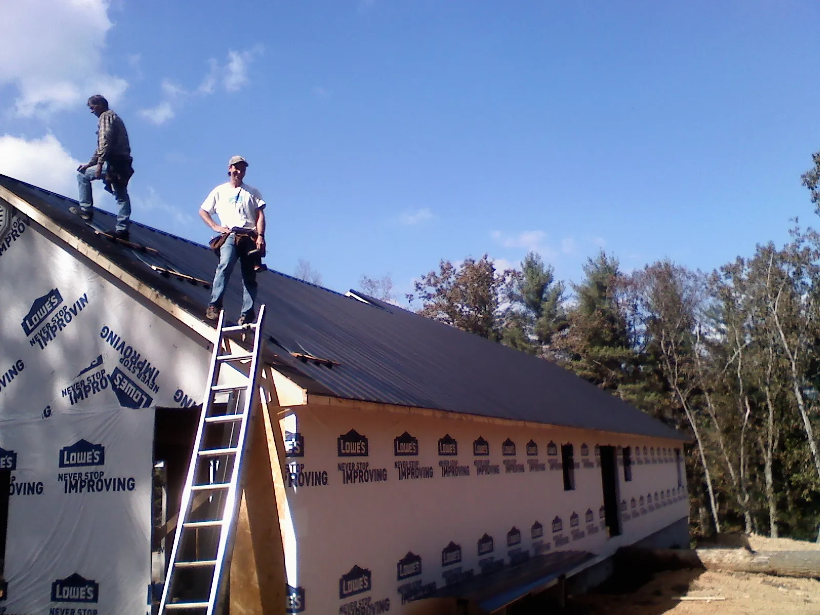 Two roofers standing on a long dark metal roof over a wrapped building in Mc Bain