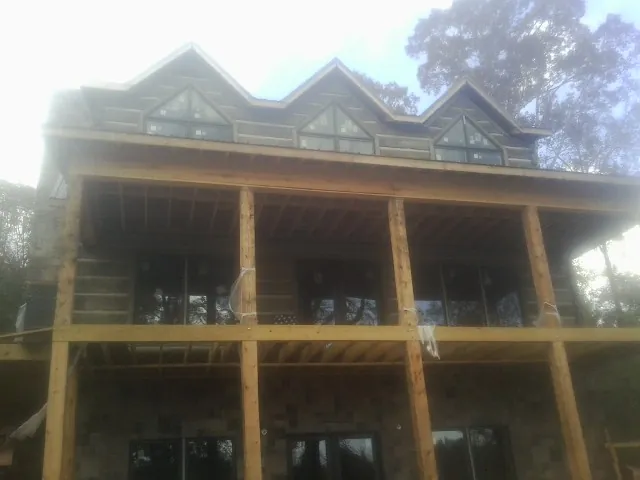 Dormers and porch framing on a large log home under construction — Roof Coating work by our crew in Mc Bain