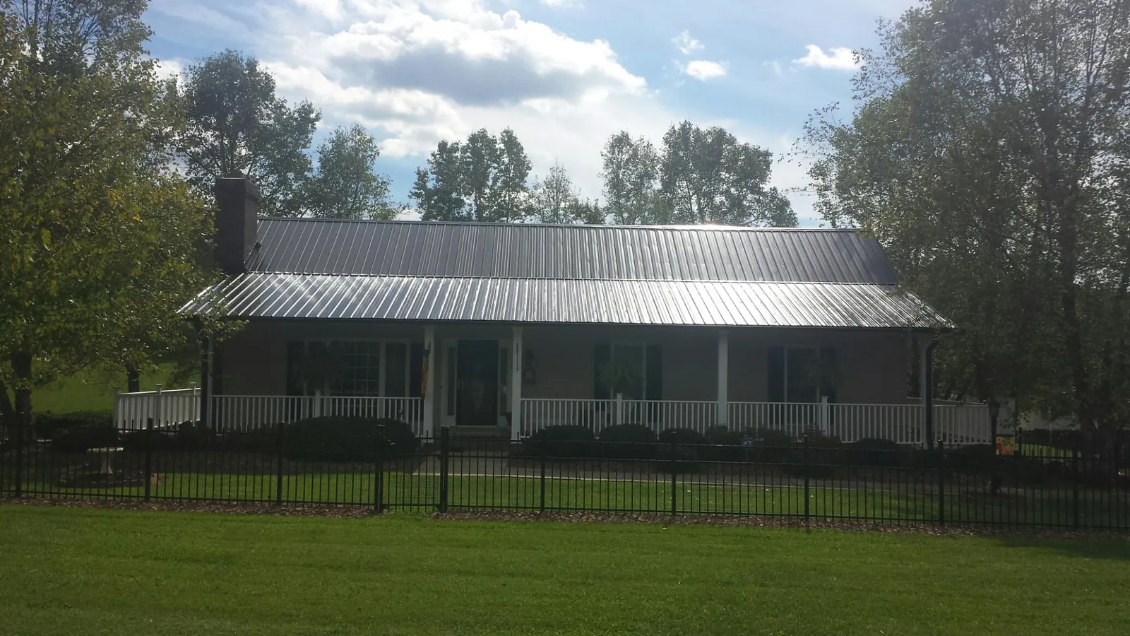 Gray metal roof on a brick ranch with a full width front porch — Gutter Guard Installation work by our crew in Mc Bain