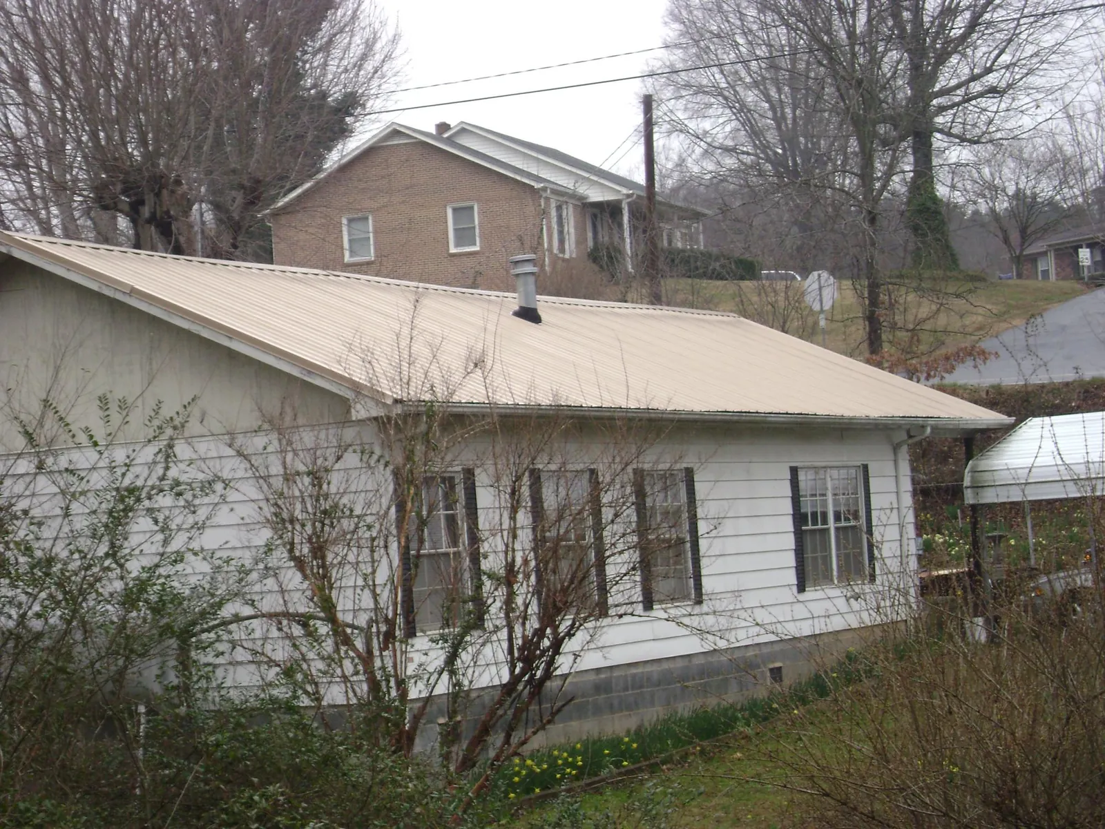 Tan metal roof on a white sided house set into a hillside — Commercial Roofing by Roofing Brothers in Mc Bain