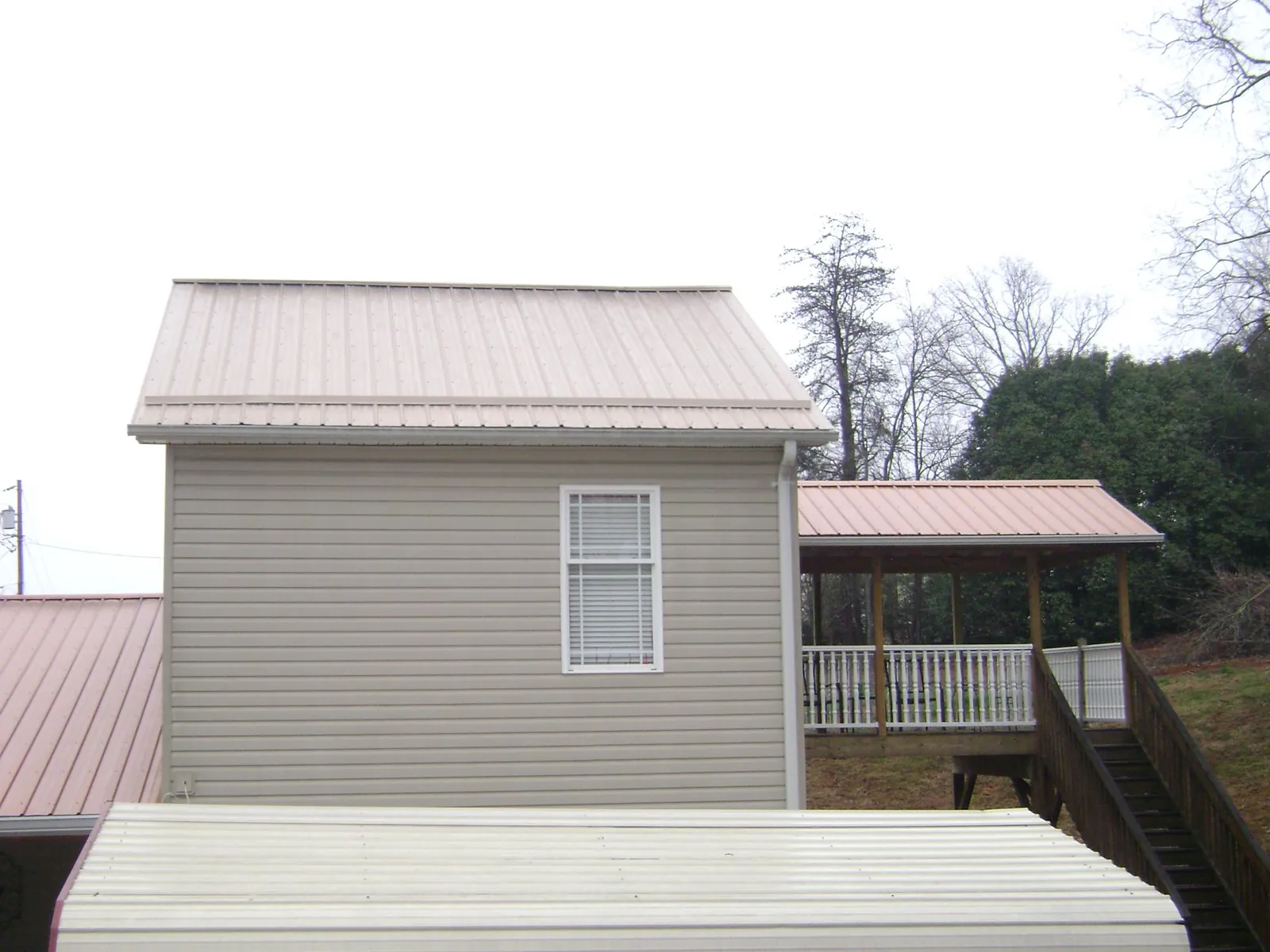 Tan metal roofs on a two story addition and attached porch, from a Roof Replacement job in Mc Bain
