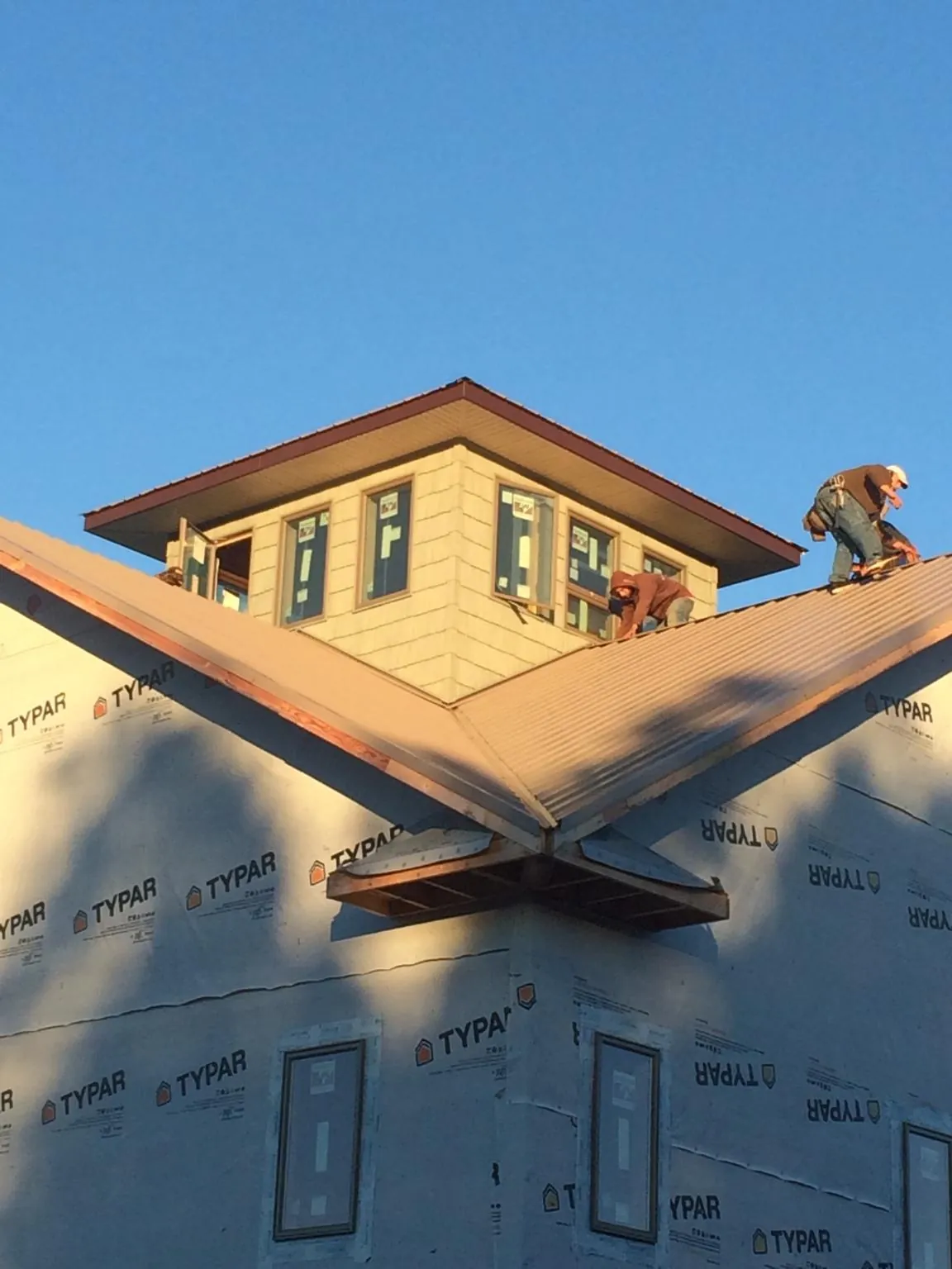Roofers working around a rooftop cupola on a new metal roof at sunset — Roof Waterproofing in Mc Bain by Roofing Brothers
